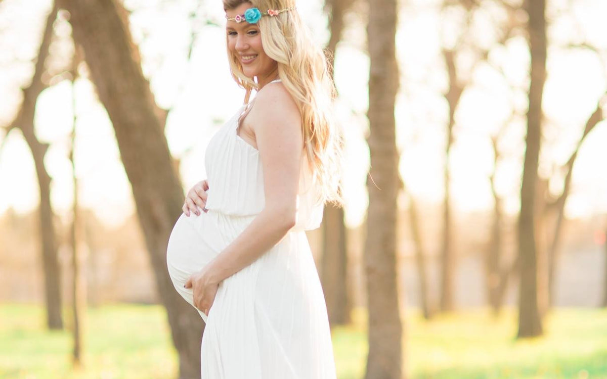 Holly Tanella, pregnant, in a white dress among trees in golden evening light