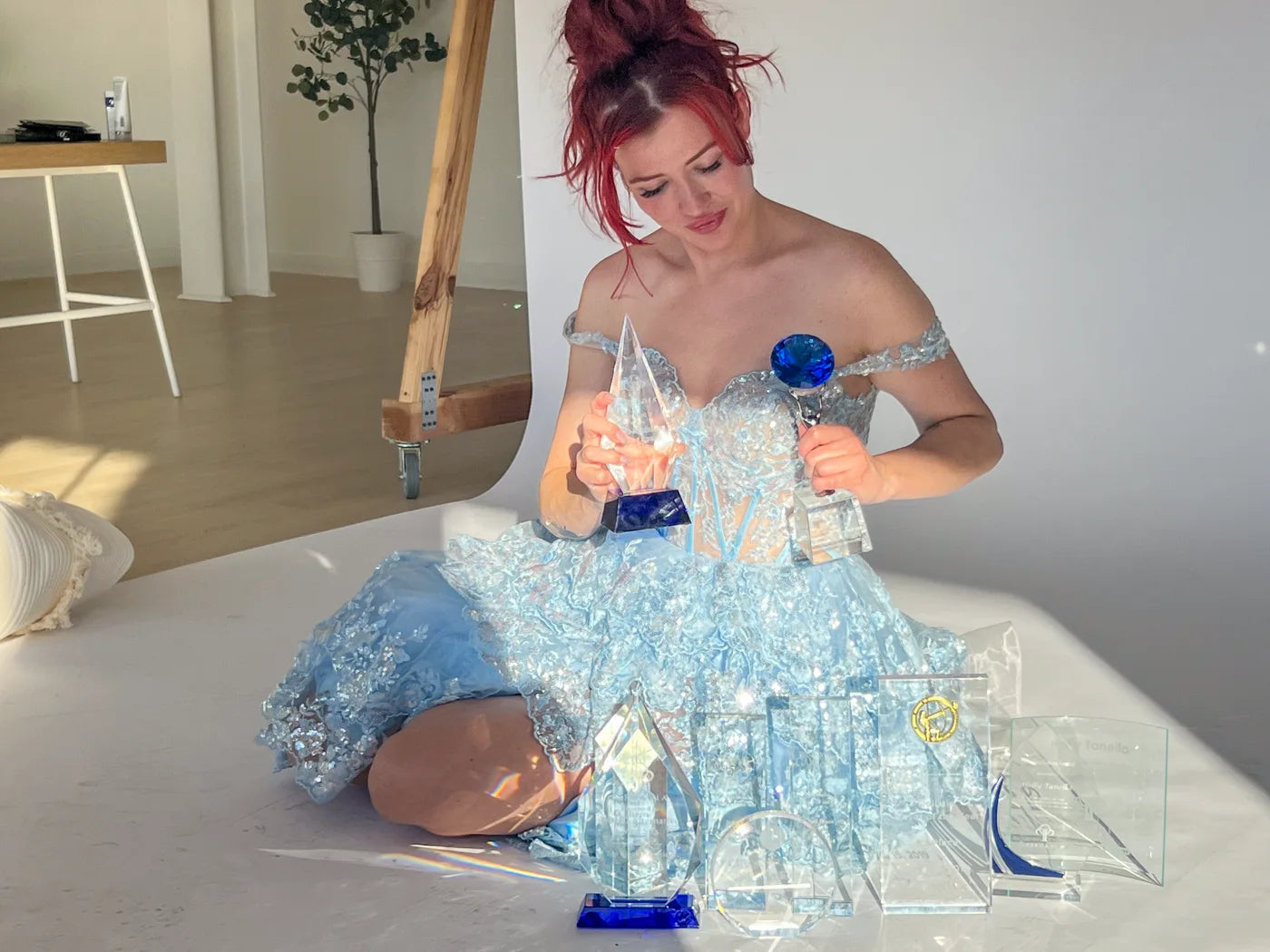 Holly Tanella holding two glass awards beside her other trophies
