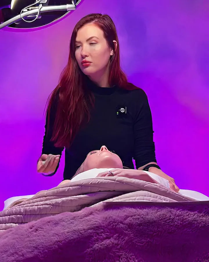 Holly Tanella at the treatment bed, resting her hands on a guest tucked under a plush blanket