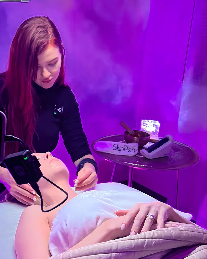 Holly Tanella leaning over a guest on the treatment bed under a soft ring light in a violet room